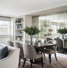 the dining room table is surrounded by chairs and vases with flowers in them, along with large mirrors on the wall