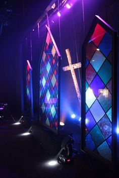 three stained glass windows in the dark with lights shining on them and a crucifix