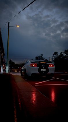 a white sports car is parked on the side of the road at night with its lights on