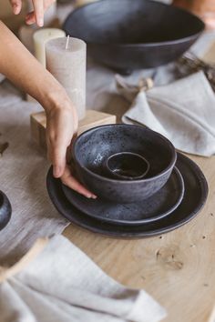 a person placing a candle in a bowl on a table with plates and napkins