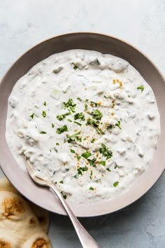 a bowl filled with white sauce and garnished with parsley next to pita bread