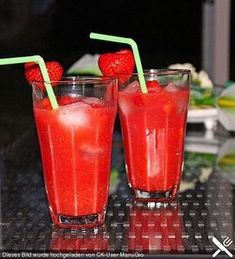 two glasses filled with red liquid and strawberries on top of each glass, sitting on a table