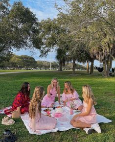 a group of young women sitting on top of a blanket in the grass eating cake