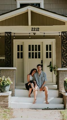 a man and woman sitting on the front steps of a house with their arms around each other