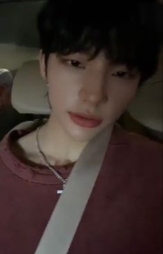 a young man sitting in the back seat of a car wearing a red shirt and silver necklace