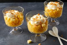 three desserts with whipped cream and nuts in small glass dishes next to spoons