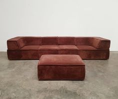 a red couch and ottoman sitting on top of a cement floor next to a white wall