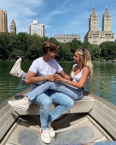 a man and woman are sitting in a boat on the water with buildings in the background