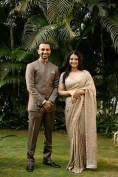 a man and woman standing next to each other in front of some palm tree leaves