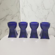 three blue glass cups sitting on top of a white table next to a marble wall