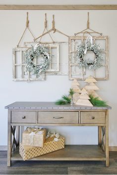 two christmas wreaths are hanging on the wall above a table with presents underneath it