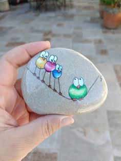 a hand holding a rock with three birds painted on it and string attached to the rocks