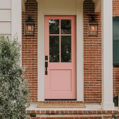 a pink front door on a brick house with two lights above it and bushes in the foreground