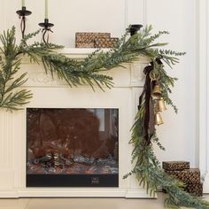 a fireplace decorated for christmas with pine branches and bells