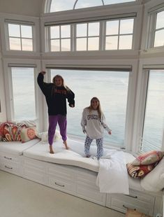 two girls are standing on a window sill in front of the ocean and one girl is holding her hand up