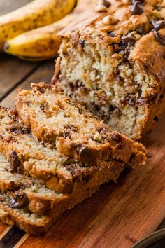 sliced loaf of banana chocolate chip bread on wooden cutting board with two bananas in the background