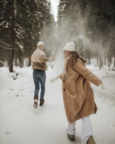 two people walking in the snow near trees