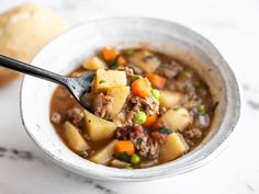 a white bowl filled with stew and potatoes on top of a table next to a piece of bread