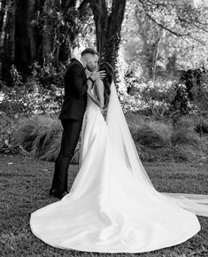 a bride and groom kissing in front of a large tree at their wedding day, black and white photo