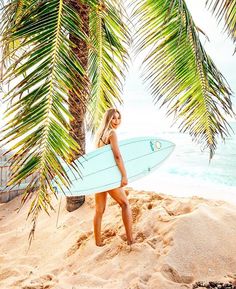 a beautiful woman holding a surfboard on top of a sandy beach