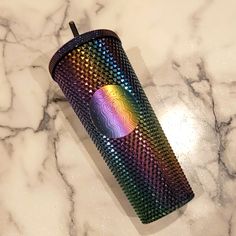 a rainbow colored cup sitting on top of a marble counter next to a cell phone