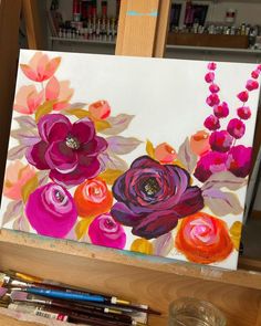 an easel with flowers painted on it and some paintbrushes next to it