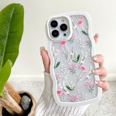 a woman holding an iphone case with pink flowers on it and green leaves in the background