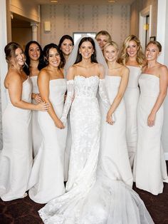 a group of women standing next to each other wearing white dresses and holding bouquets