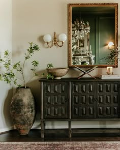 a room with a mirror, vases and a plant on the sideboard in front of it