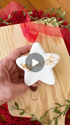 a person holding a star shaped object on top of a wooden board with red ribbon