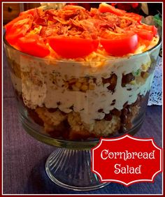 a layered cake with tomatoes on top and cornbread salad in the middle, sitting on a glass pedestal