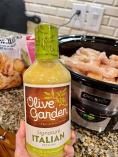 a hand holding a bottle of olive garden italian dressing in front of an instant pressure cooker