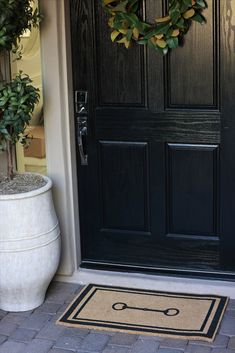 a black door with a wreath on it and a potted plant next to it