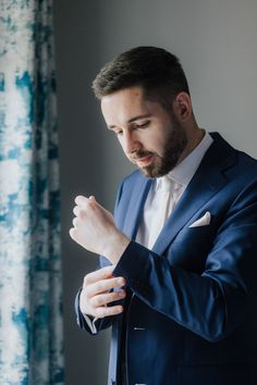 a man in a blue suit and white shirt is looking down at his hands as he adjusts his tie