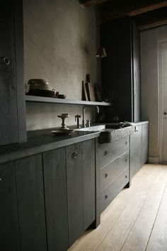 an empty kitchen with wooden floors and black cabinets in front of a door that leads to another room