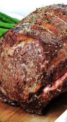 a large piece of meat sitting on top of a wooden cutting board next to green beans