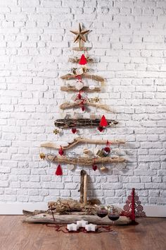 a christmas tree made out of driftwood on a wooden floor in front of a white brick wall