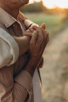 an older man holding his hands together while standing on the side of a dirt road