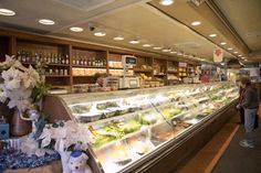 a woman standing in front of a deli filled with lots of food