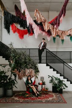 two people are sitting on the floor in front of some plants and hanging streamers