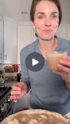 a woman holding a glass in her hand while standing next to a pan filled with food