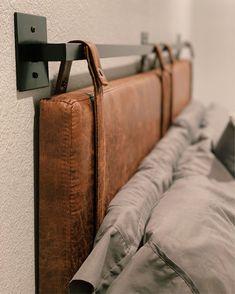 a bed with a brown leather headboard hanging from it's side next to a white wall