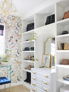 a room with white shelves filled with purses and shoes on top of them next to a blue chair