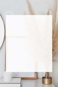 a white table topped with a vase filled with dry grass next to a round mirror