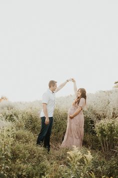 a man and woman holding hands while standing in tall grass