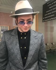 a man in a suit and hat looks down at his cell phone while wearing sunglasses