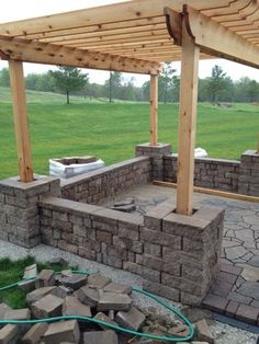 an outdoor patio with stone walls and brick seating area under a pergolated roof