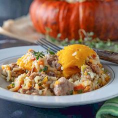 a white plate topped with rice and meat next to a pumpkin on a wooden table