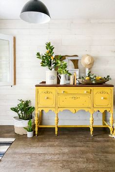 a yellow dresser sitting on top of a hard wood floor next to potted plants