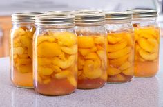 four glass jars filled with sliced peaches on a countertop in a kitchen or dining room